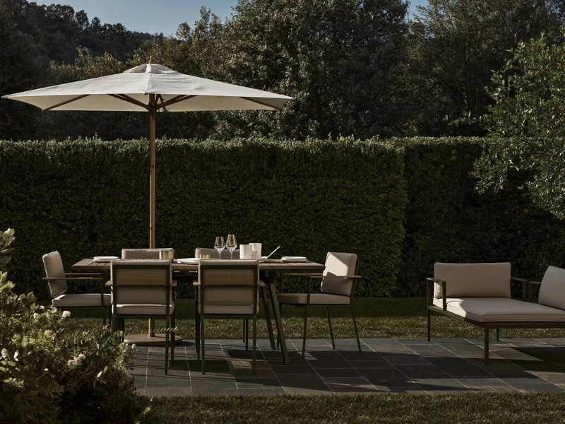 Illustrierte Gartenterrasse mit Esstisch, Loungeecke und Sonnenschirm vor Rasen und Hecke
